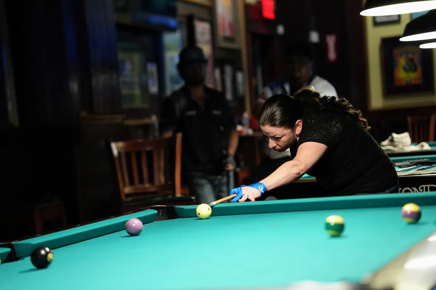 A player down on a shot along the rail during the 8-Ball final, cue lined up on the cue ball with the rest of the table out of focus.