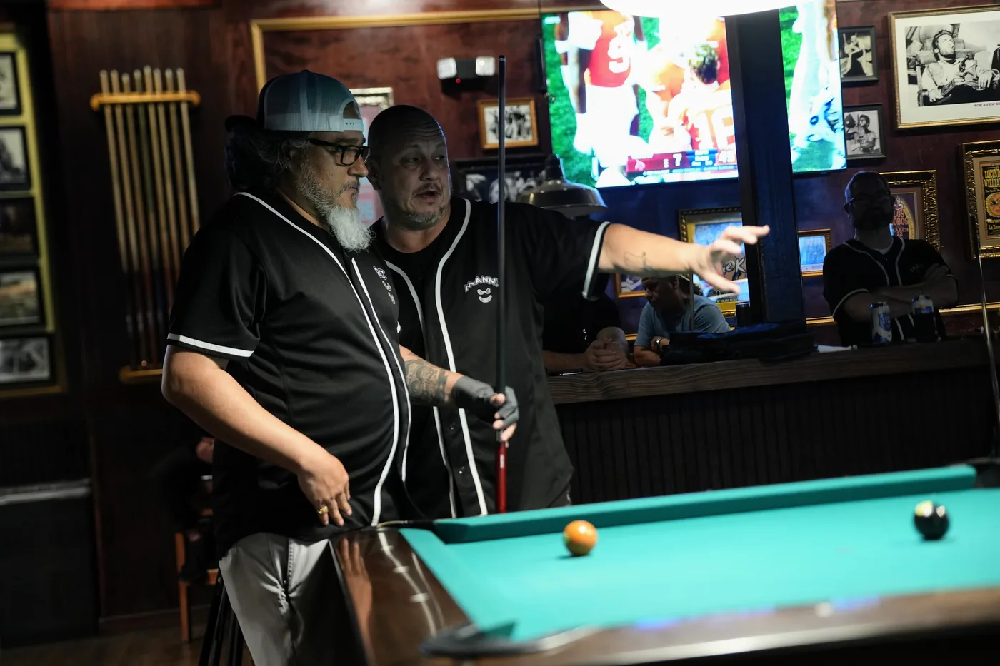 Two teammates in matching black jerseys talking through the table from the rail between shots at the 8-Ball qualifier.